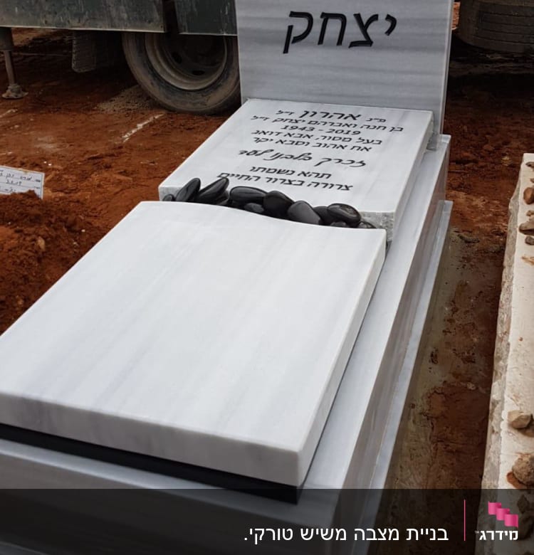 מצבה עם כיתוב בעברית ואבנים שחורות